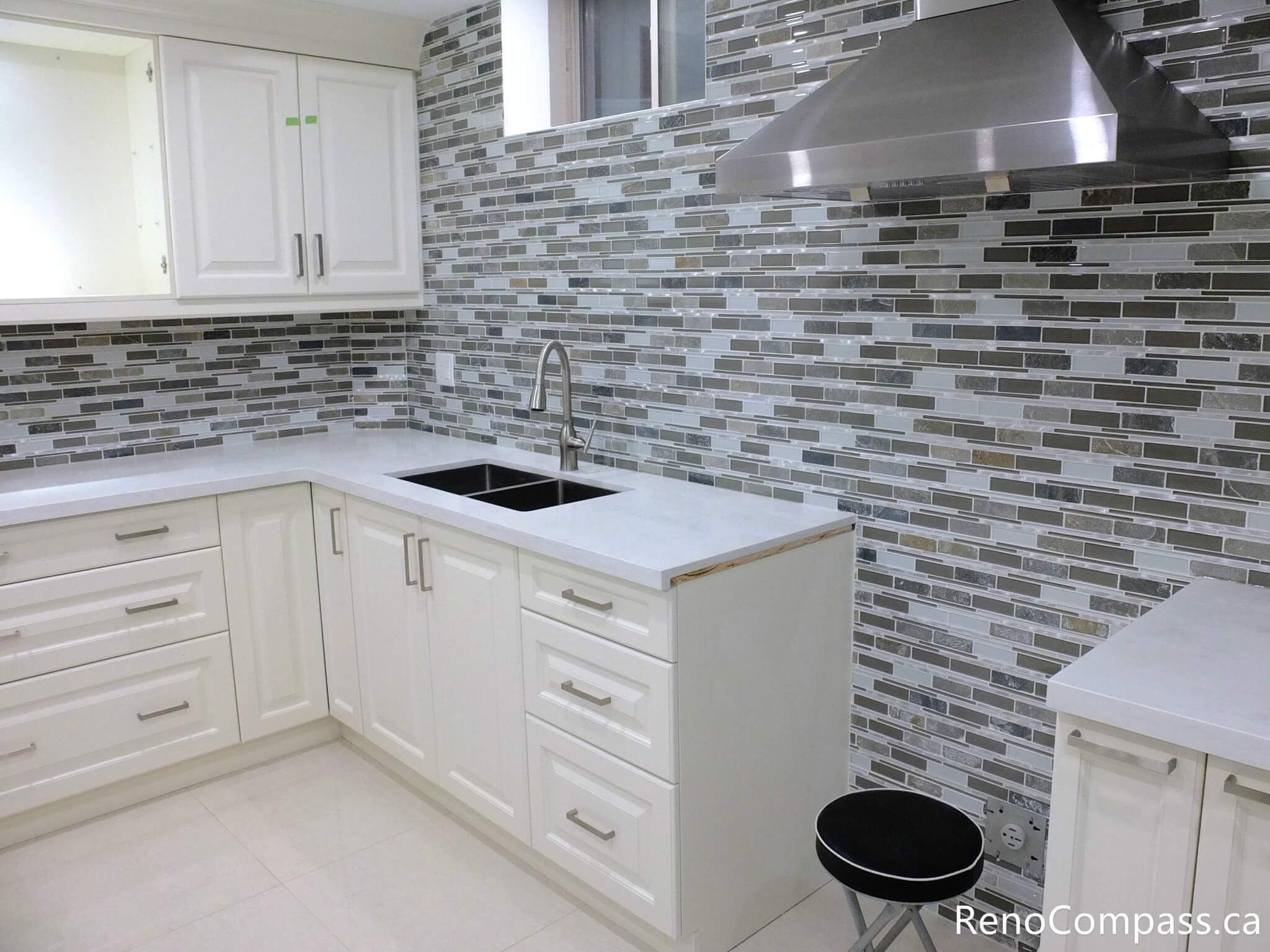 This Markham basement kitchen features elegant white shaker cabinets paired with a full-height mosaic tile backsplash, creating a clean and modern visual contrast. The stainless steel range hood, under-counter storage, and functional layout make this space both stylish and practical for everyday use or rental purposes. Completed by a reliable Toronto Renovation Company, Reno Compass Inc.