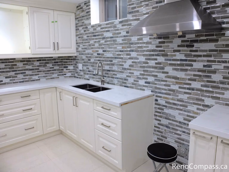 This Markham basement kitchen features elegant white shaker cabinets paired with a full-height mosaic tile backsplash, creating a clean and modern visual contrast. The stainless steel range hood, under-counter storage, and functional layout make this space both stylish and practical for everyday use or rental purposes. Completed by a reliable Toronto Renovation Company, Reno Compass Inc.