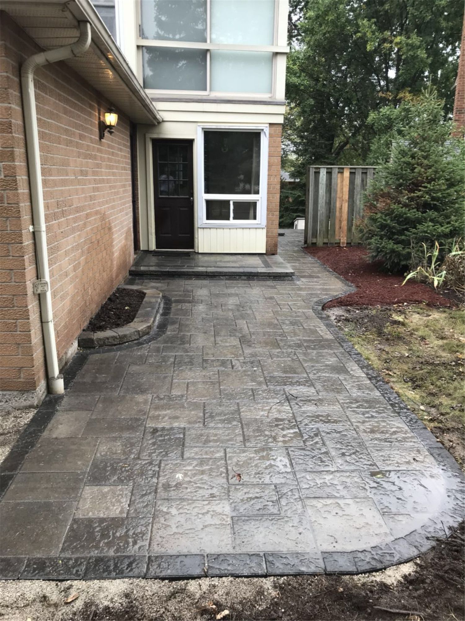 Backyard landscaping project in Toronto featuring a custom interlocking patio and curved garden pathway leading to the rear entrance. The design improves accessibility, drainage, and outdoor functionality while creating a clean and modern backyard landscape.