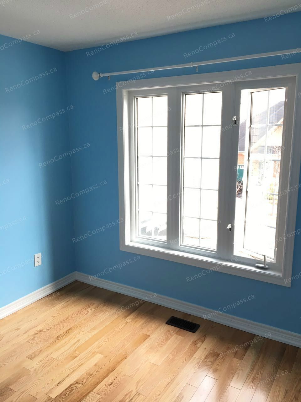 This Markham interior renovation showcases a refreshed bedroom with smooth blue wall finishes, upgraded trim, and warm hardwood flooring. Large windows bring in natural light, creating a bright and comfortable living space. Completed by a trusted Toronto renovation company, the project enhances both visual appeal and everyday comfort through clean finishes and modern detailing.