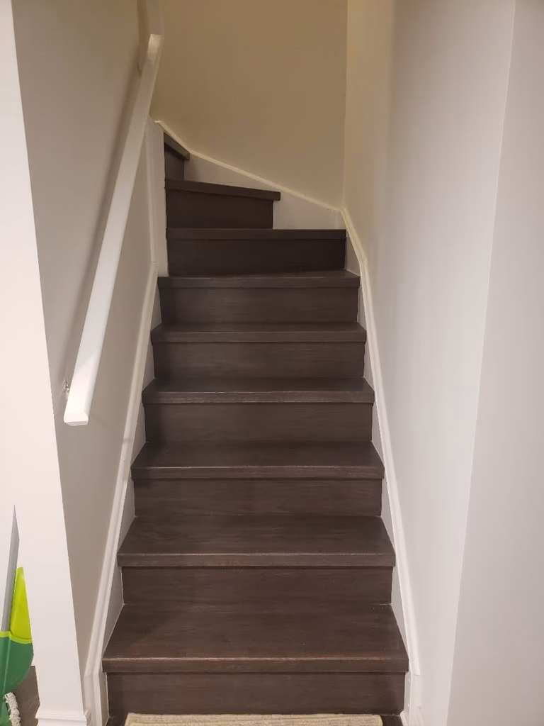 This Markham basement renovation includes a staircase upgrade featuring durable dark wood steps and clean white railings for a modern, streamlined look. The refreshed stair design enhances safety and visual continuity between the main floor and the finished basement. Neutral wall tones and updated trim create a bright, cohesive transition space while maximizing durability for daily use. This professionally completed staircase renovation reflects quality craftsmanship and thoughtful design, adding both function and aesthetic value to the overall Markham basement renovation project.
