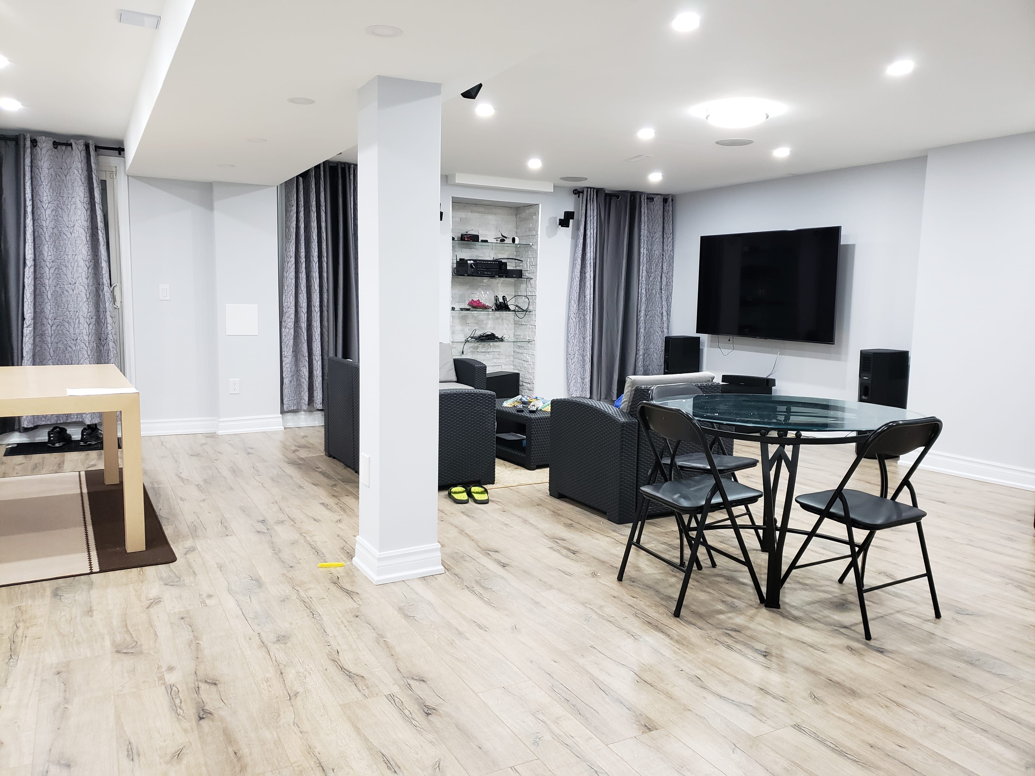 This newly finished basement renovation in Newmarket, Toronto features a bright open-concept layout with upgraded flooring, recessed pot lights, and a modern entertainment area. The space includes a comfortable lounge zone, dining table setup, and custom lighting design that enhances both functionality and visual comfort. Large curtains and neutral wall tones create a clean, contemporary atmosphere, making the basement ideal for family gatherings and everyday living. Professionally completed by a trusted Toronto renovation company, this basement transformation focuses on durability, space optimization, and modern interior aesthetics for long-term use.