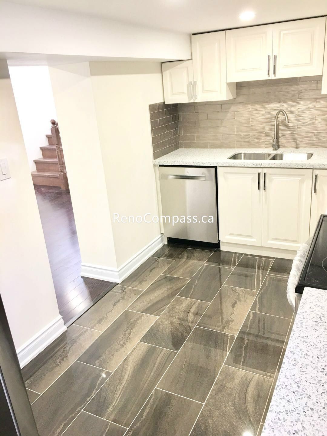 This Toronto basement renovation showcases a modern kitchenette with custom white shaker cabinets, quartz countertop, and a stylish textured backsplash. The compact layout includes a double sink, built-in microwave space, and durable tile flooring, creating a clean and functional secondary kitchen. Completed by a trusted Toronto renovation company, this basement kitchen upgrade adds convenience, value, and contemporary appeal to the home.