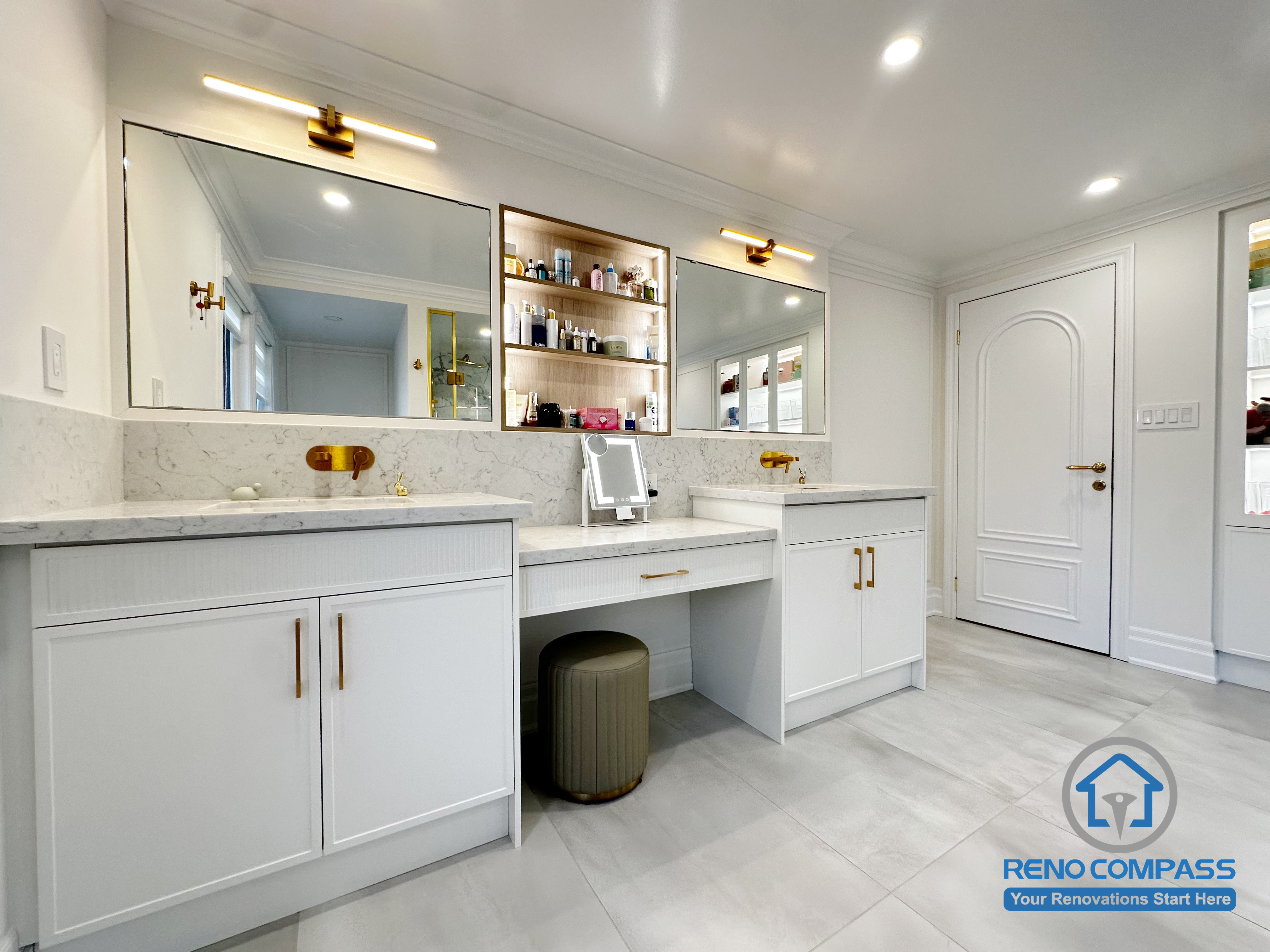 This Markham bathroom renovation showcases a symmetrical double vanity design paired with a built-in central storage niche and makeup area. Custom cabinetry on both sides ensures balanced storage, while integrated mirrors and warm-toned fixtures enhance visual cohesion. The layout prioritizes daily functionality, clean circulation, and a refined, organized appearance—creating a bathroom that feels both practical and thoughtfully designed for shared use.