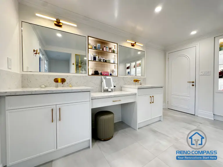 This Markham bathroom renovation showcases a symmetrical double vanity design paired with a built-in central storage niche and makeup area. Custom cabinetry on both sides ensures balanced storage, while integrated mirrors and warm-toned fixtures enhance visual cohesion. The layout prioritizes daily functionality, clean circulation, and a refined, organized appearance—creating a bathroom that feels both practical and thoughtfully designed for shared use.