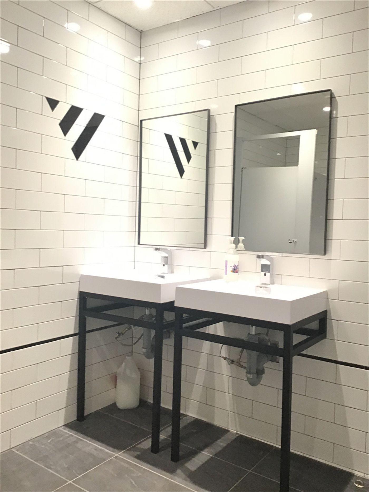 Modern commercial washroom renovation in downtown Toronto featuring double vanity sinks, white subway tile walls, black metal framing, and clean functional design ideal for office or retail spaces.