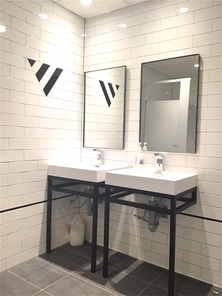 Modern commercial washroom renovation in downtown Toronto featuring double vanity sinks, white subway tile walls, black metal framing, and clean functional design ideal for office or retail spaces.