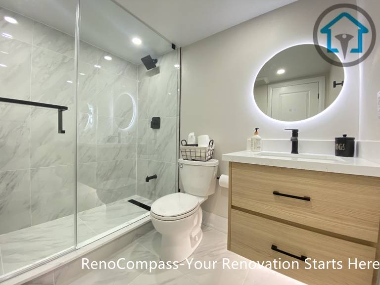 本地下室浴室由 Reno Compass 施工团队完成整体翻新与升级。空间采用现代简约设计，配置步入式玻璃淋浴房，搭配大规格墙地砖与黑色五金配件，在保证防水与耐用性的同时提升整体质感。定制洗手台结合悬挂式圆形灯镜，优化照明效果并增强空间层次。通过合理布局洁具与收纳，使有限的地下室浴室在实用性、舒适度与视觉整洁度之间取得平衡，满足家庭长期使用需求。