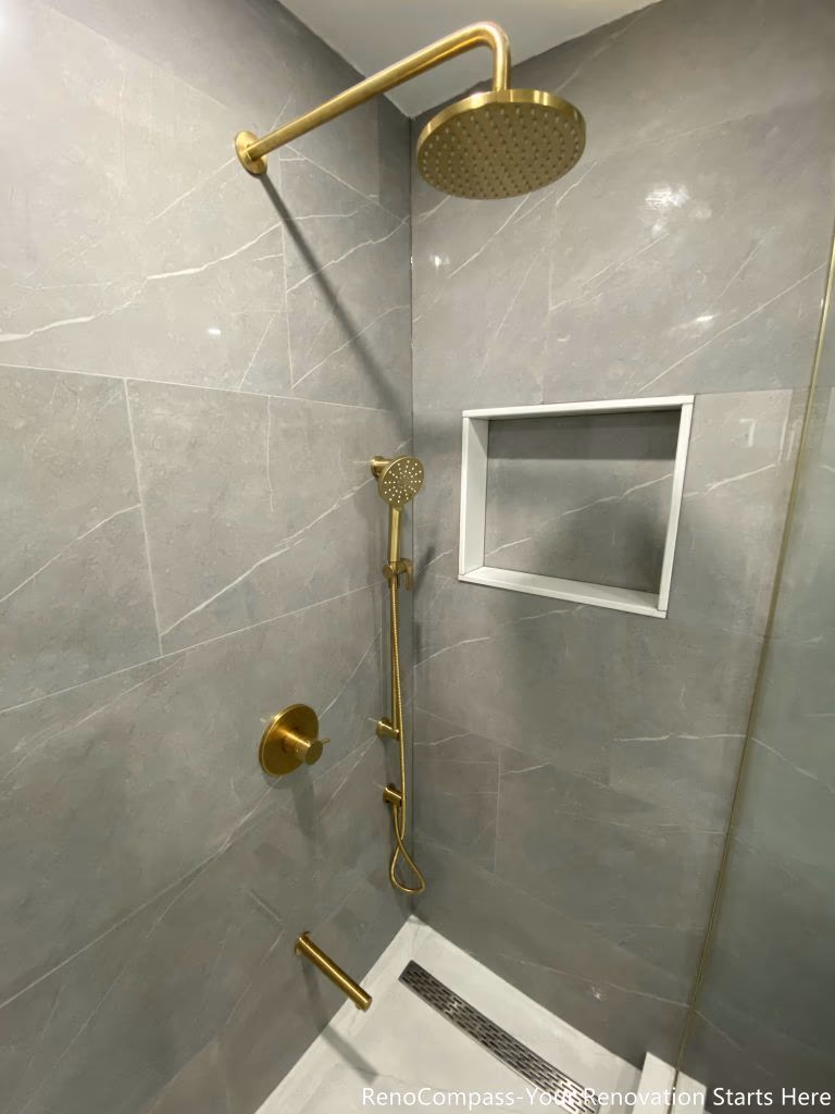 This Oakville master bathroom renovation features a sleek walk-in shower with premium gold rain shower system and modern handheld fixture for a luxury spa-like experience. Large-format marble-look wall tiles, a built-in recessed shower niche, and a linear floor drain create a clean, contemporary design with enhanced functionality. Completed by a professional Toronto renovation company, this bathroom upgrade combines elegant finishes, efficient drainage, and durable materials to deliver both comfort and long-term value for the homeowner.