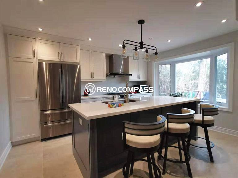 This modern kitchen island is part of a North York interior renovation, designed as a central gathering and working space for daily living. The oversized island features a quartz countertop with an undermount sink, paired with custom cabinetry and integrated seating. Black industrial-style pendant lights create visual contrast against the light cabinetry, while recessed ceiling lighting ensures balanced illumination throughout the space. Stainless steel appliances and a clean backsplash complete the contemporary look, reflecting the craftsmanship and design quality expected from a professional Toronto interior renovation project.