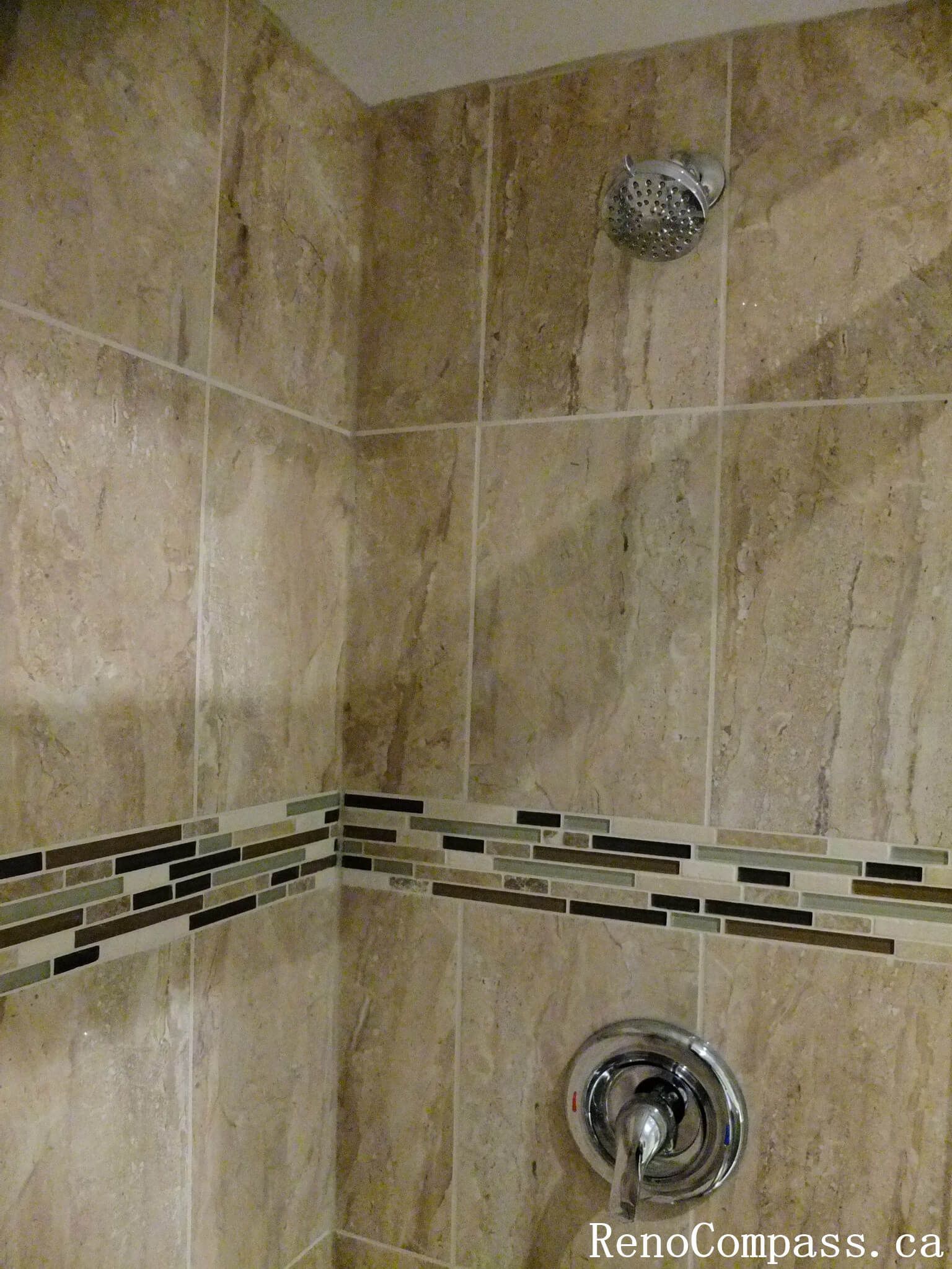 Shower area detail from a North York bathroom renovation, featuring full-height wall tiles, mosaic accent band, and slip-resistant floor tiles with clean grout lines and precise craftsmanship.