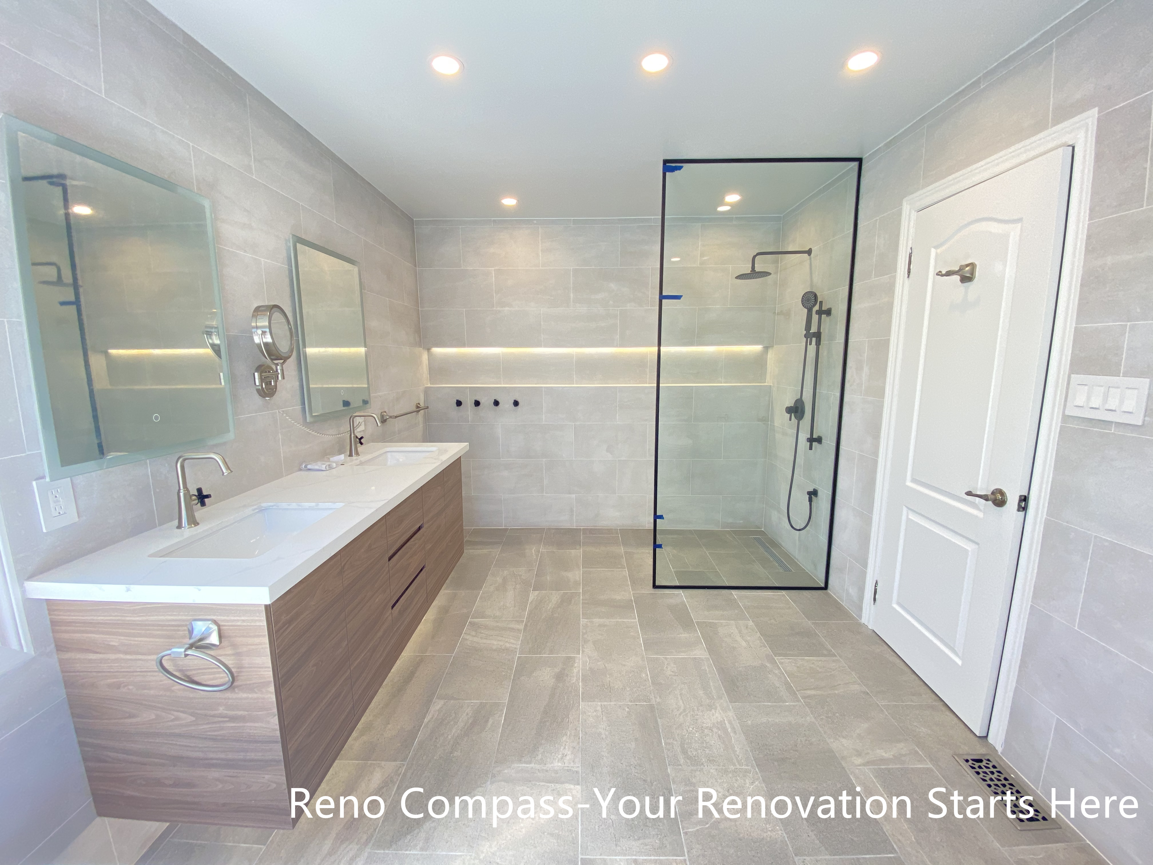 This Aurora bathroom renovation showcases a well-balanced layout featuring a double-sink vanity with warm wood finishes and a modern walk-in shower enclosed in clear glass. Large-format tiles across the floor and walls create a cohesive visual flow, while integrated niche lighting and recessed ceiling lights enhance brightness throughout the space. The arrangement supports efficient daily use with clear circulation and ample storage, resulting in a bathroom that feels open, refined, and practical. Designed and completed by Reno Compass, this renovation emphasizes clarity, comfort, and long-term functionality.
