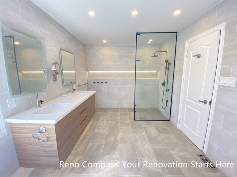 This Aurora bathroom renovation showcases a well-balanced layout featuring a double-sink vanity with warm wood finishes and a modern walk-in shower enclosed in clear glass. Large-format tiles across the floor and walls create a cohesive visual flow, while integrated niche lighting and recessed ceiling lights enhance brightness throughout the space. The arrangement supports efficient daily use with clear circulation and ample storage, resulting in a bathroom that feels open, refined, and practical. Designed and completed by Reno Compass, this renovation emphasizes clarity, comfort, and long-term functionality.