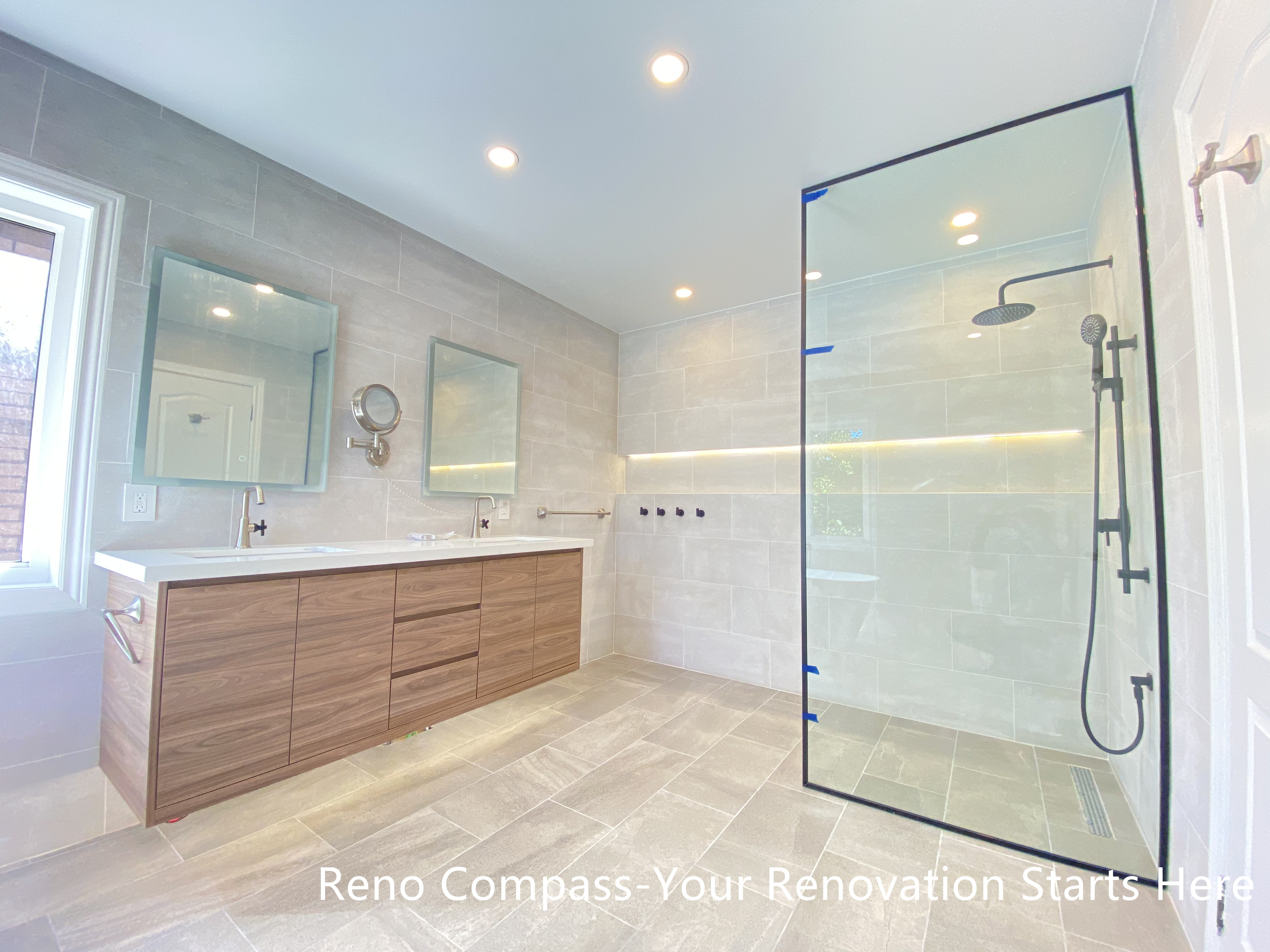 This Aurora bathroom renovation showcases a well-balanced layout featuring a double-sink vanity with warm wood finishes and a modern walk-in shower enclosed in clear glass. Large-format tiles across the floor and walls create a cohesive visual flow, while integrated niche lighting and recessed ceiling lights enhance brightness throughout the space. The arrangement supports efficient daily use with clear circulation and ample storage, resulting in a bathroom that feels open, refined, and practical. Designed and completed by Reno Compass, this renovation emphasizes clarity, comfort, and long-term functionality.