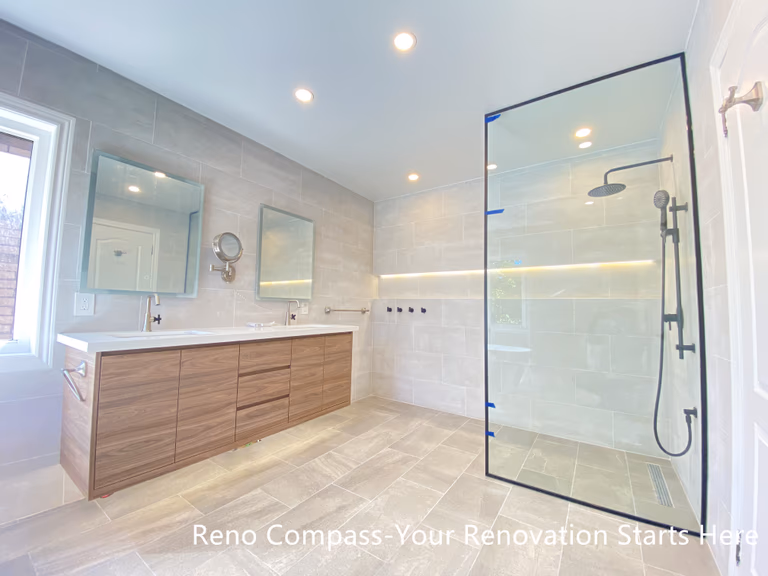 This Aurora bathroom renovation showcases a well-balanced layout featuring a double-sink vanity with warm wood finishes and a modern walk-in shower enclosed in clear glass. Large-format tiles across the floor and walls create a cohesive visual flow, while integrated niche lighting and recessed ceiling lights enhance brightness throughout the space. The arrangement supports efficient daily use with clear circulation and ample storage, resulting in a bathroom that feels open, refined, and practical. Designed and completed by Reno Compass, this renovation emphasizes clarity, comfort, and long-term functionality.