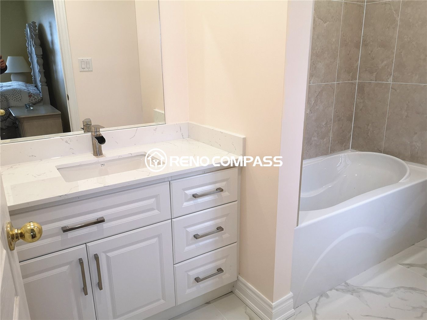 This elegant Toronto bathroom renovation showcases a modern white vanity with a quartz countertop and stylish chrome handles. The built-in bathtub features a sleek tiled wall surround, combining durability with sophistication. Designed by Reno Compass, this project highlights clean lines and functional beauty for a contemporary home upgrade.