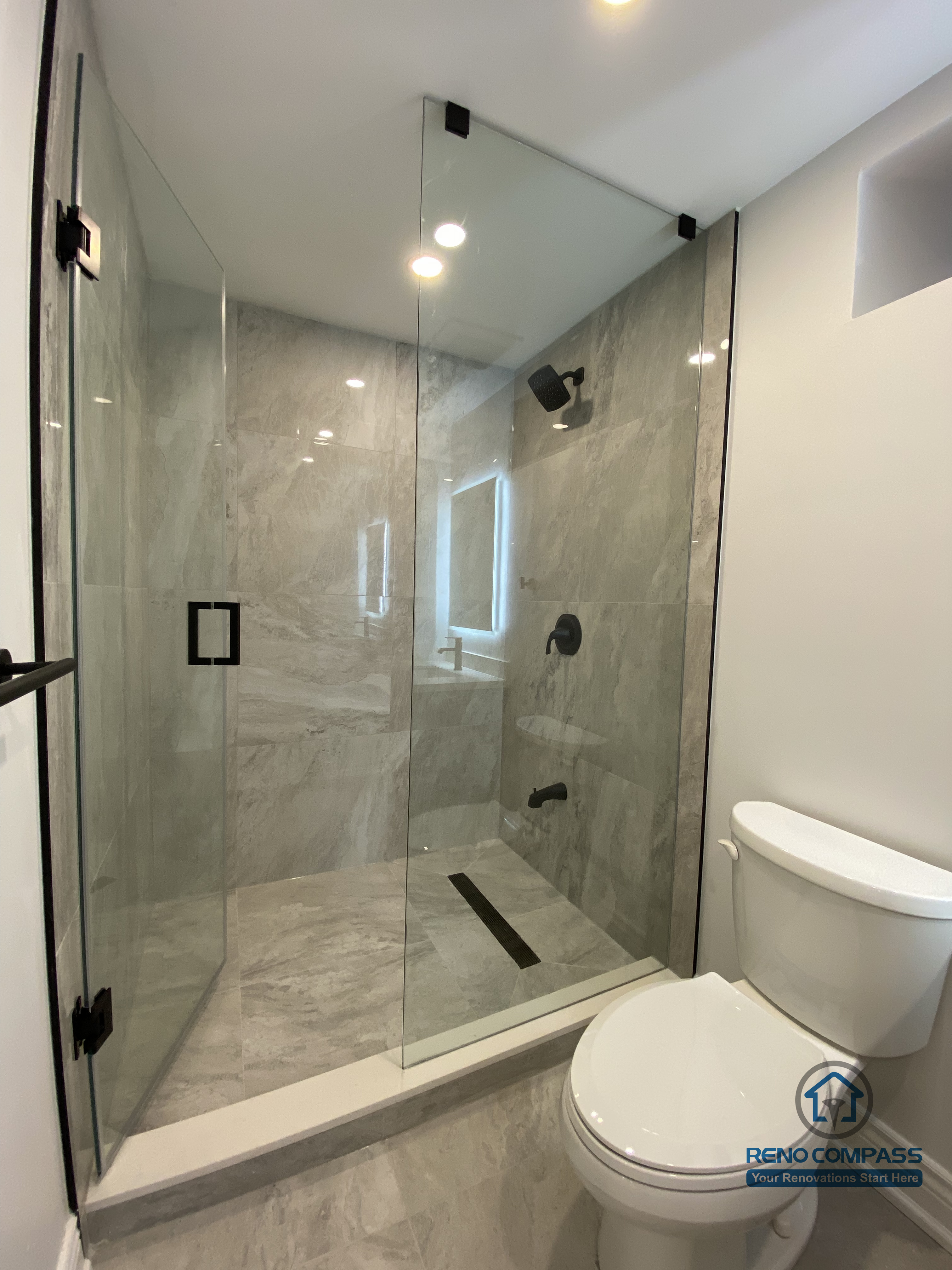 This Markham bathroom renovation features a modern walk-in shower with frameless glass panels and large-format marble-style porcelain tiles. The extended shower layout improves daily usability while maintaining a clean, open visual flow. Black shower fixtures, a linear floor drain, and full-height wall tiling create a refined, contemporary look with strong durability and easy maintenance. Designed and built by a professional Toronto renovation company, this bathroom upgrade balances functionality, waterproof performance, and long-term aesthetic value for residential homes.