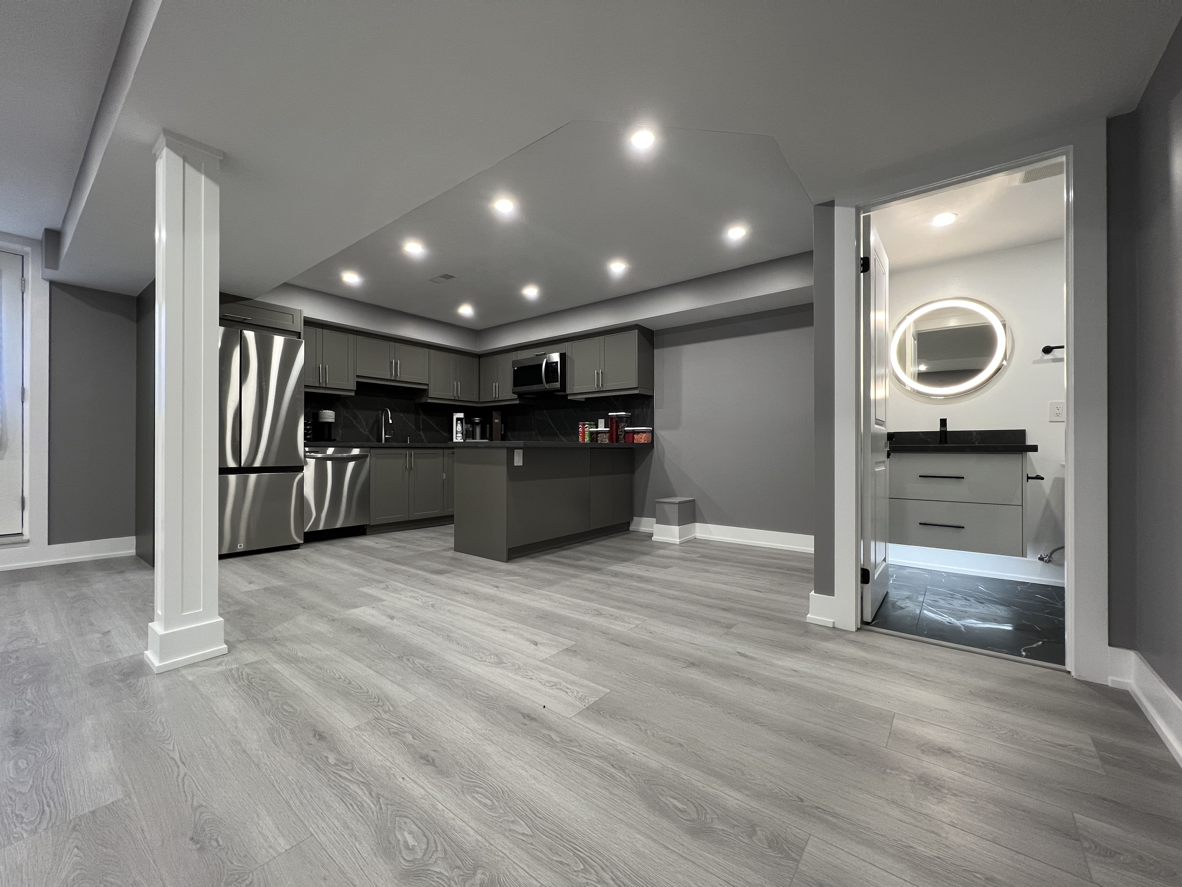 This Vaughan basement renovation features a wide open-concept layout with clear circulation, structural support columns, recessed ceiling lighting, and durable wood-look flooring. The design connects the kitchen area with flexible living and activity zones while maintaining strong structural organization and visual balance. Completed by a Toronto renovation company, this basement renovation highlights efficient space planning and modern finishes suited for multi-purpose lower-level living.