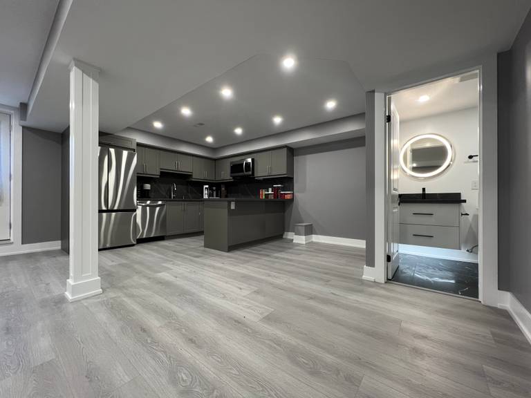 This Vaughan basement renovation features a wide open-concept layout with clear circulation, structural support columns, recessed ceiling lighting, and durable wood-look flooring. The design connects the kitchen area with flexible living and activity zones while maintaining strong structural organization and visual balance. Completed by a Toronto renovation company, this basement renovation highlights efficient space planning and modern finishes suited for multi-purpose lower-level living.