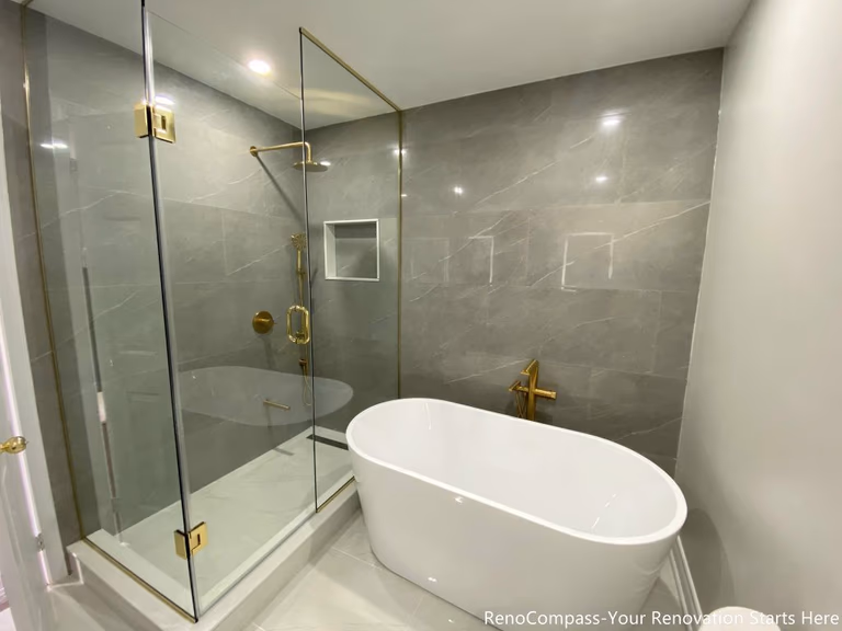 This Oakville master bathroom renovation features a sleek freestanding bathtub paired with premium gold floor-mounted fixtures and large-format marble-look wall tiles. The clean layout integrates a glass-enclosed shower and modern toilet placement, creating a functional yet luxurious spa-style bathroom environment. Completed by a professional Toronto renovation company, this upgrade enhances comfort, improves space efficiency, and delivers a timeless modern design that increases both daily living quality and overall property value.