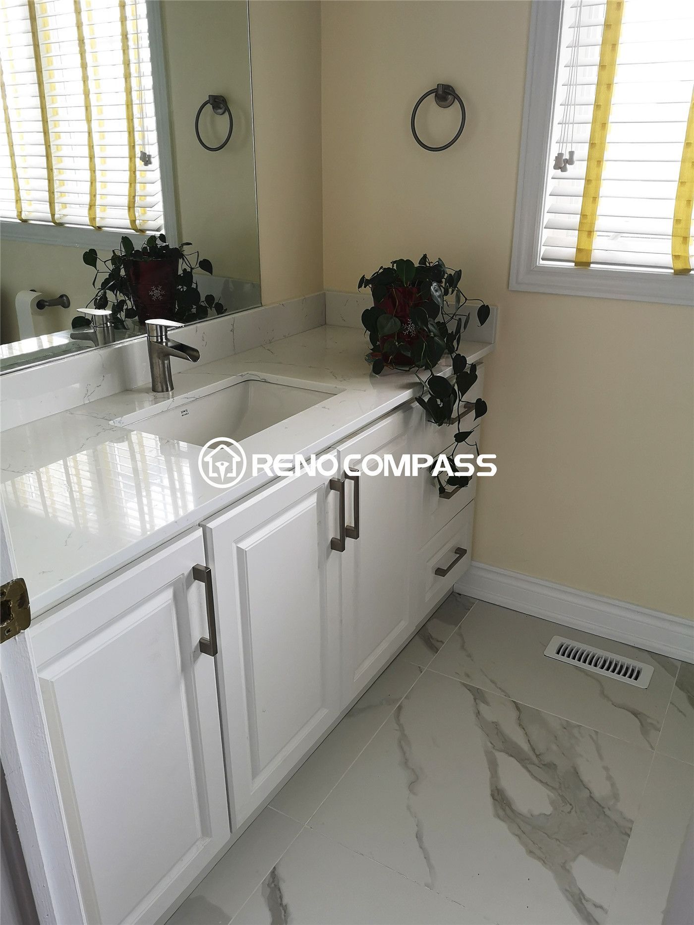 This bright Toronto bathroom renovation showcases a white vanity with a polished quartz countertop and modern chrome hardware. The space is elevated by large marble-look floor tiles and warm natural light, creating a clean and timeless aesthetic. Completed by Reno Compass, this remodel blends contemporary elegance with everyday functionality.
