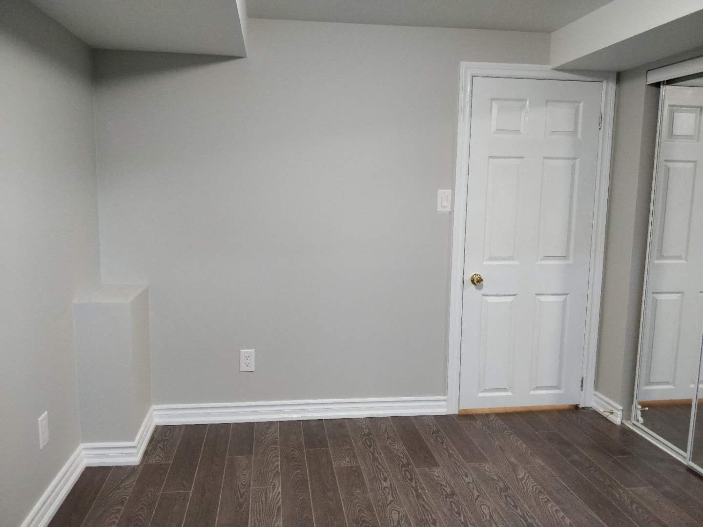 This Scarborough basement renovation showcases a finished room with modern hardwood flooring, freshly painted walls, and built-in closet space with sliding mirrored doors. The clean design and neutral color palette create a bright and practical basement bedroom or multi-purpose living area, completed by a professional Toronto renovation company.
