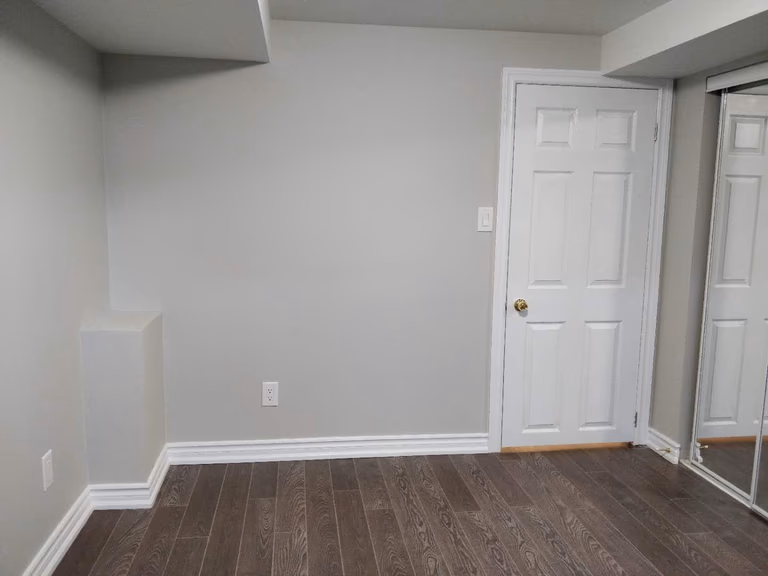 This Scarborough basement renovation showcases a finished room with modern hardwood flooring, freshly painted walls, and built-in closet space with sliding mirrored doors. The clean design and neutral color palette create a bright and practical basement bedroom or multi-purpose living area, completed by a professional Toronto renovation company.