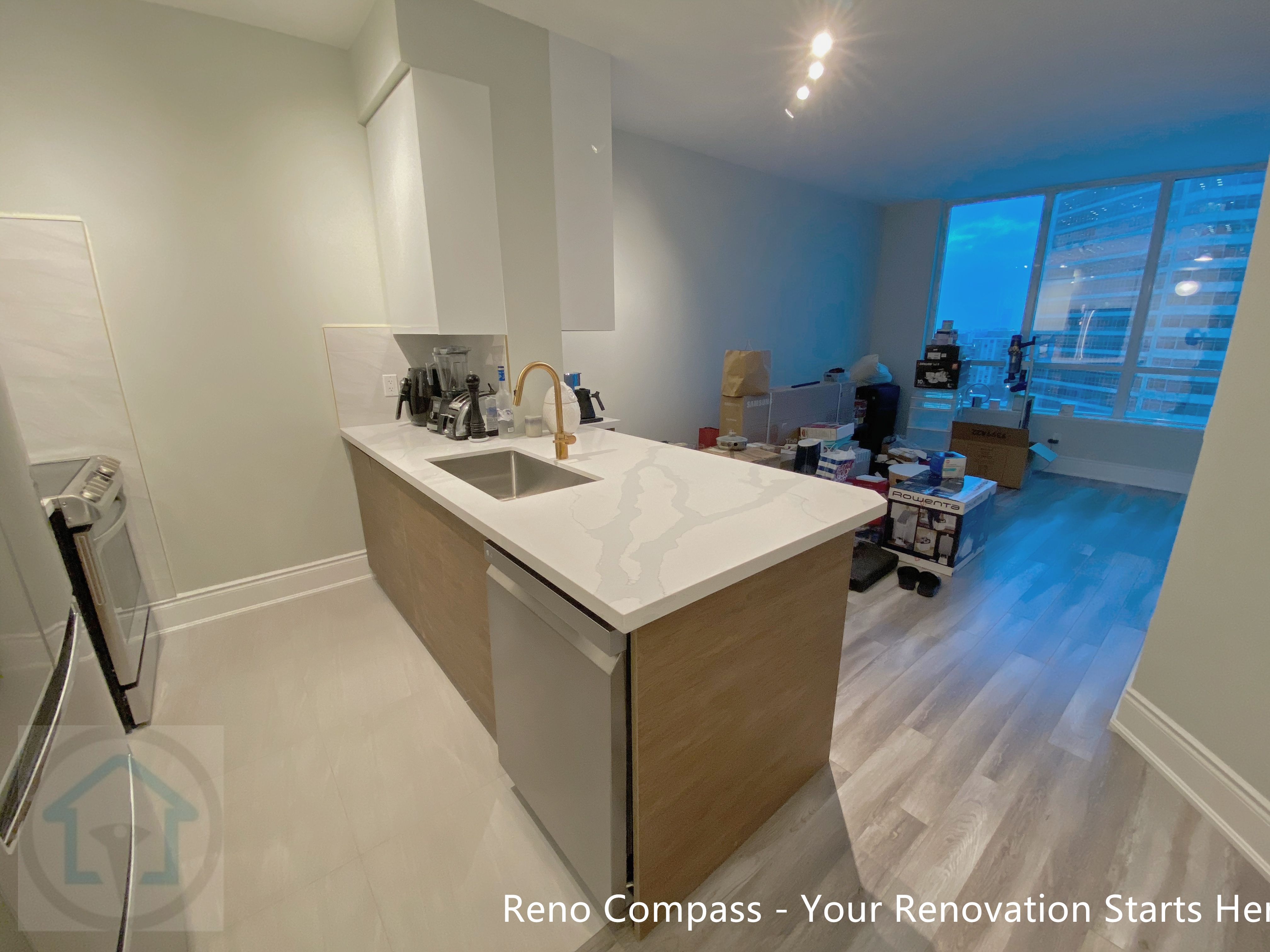 This North York condo kitchen renovation showcases a modern layout centered around a quartz waterfall island with integrated seating. White flat-panel cabinetry, stainless steel appliances, and a warm wood base create a balanced contrast between clean lines and natural tones. The redesigned kitchen improves storage efficiency, workflow, and everyday functionality, making it ideal for contemporary condo living and long-term value.