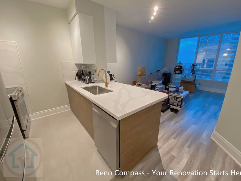 This North York condo kitchen renovation showcases a modern layout centered around a quartz waterfall island with integrated seating. White flat-panel cabinetry, stainless steel appliances, and a warm wood base create a balanced contrast between clean lines and natural tones. The redesigned kitchen improves storage efficiency, workflow, and everyday functionality, making it ideal for contemporary condo living and long-term value.
