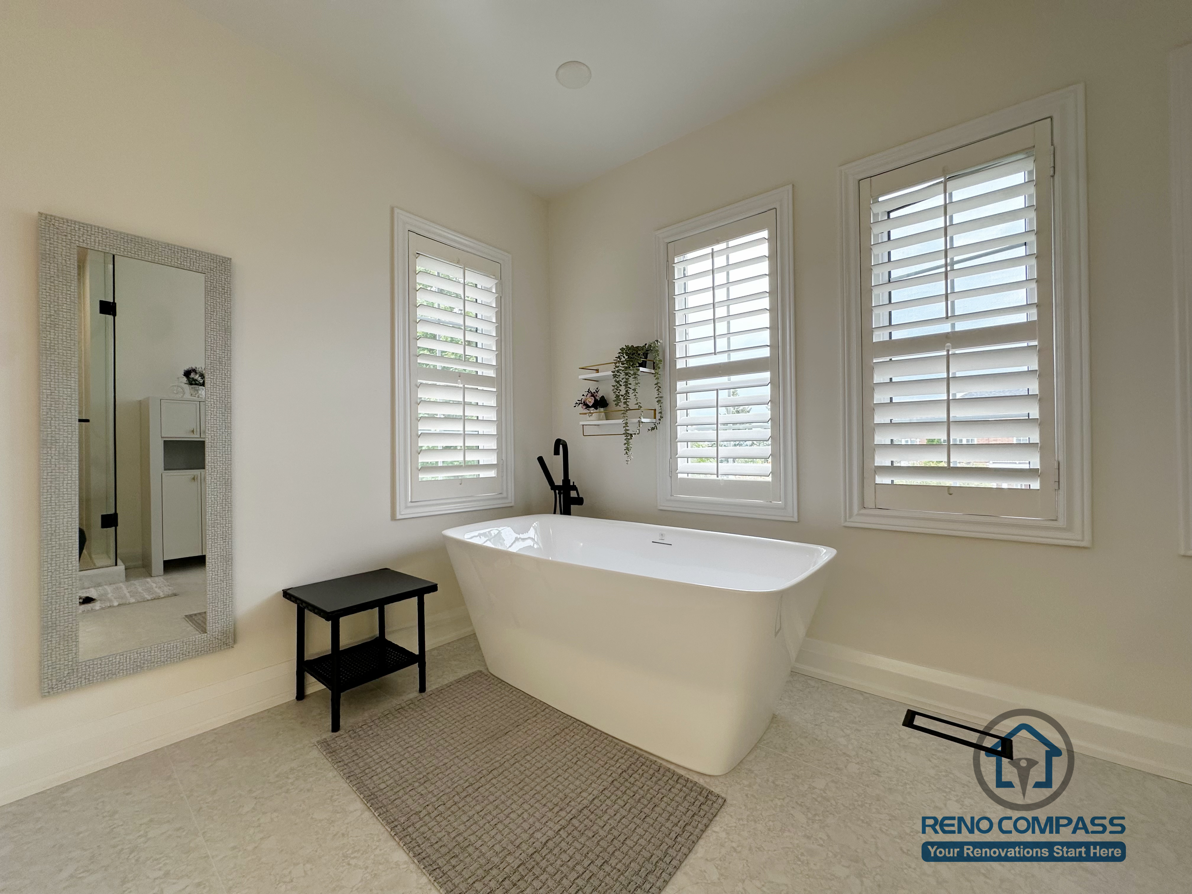 This Markham bathroom renovation features a freestanding soaking tub positioned between large windows with plantation shutters. The clean layout, soft neutral palette, and minimal black accents create a calm, spa-inspired atmosphere focused on comfort, light flow, and everyday relaxation.