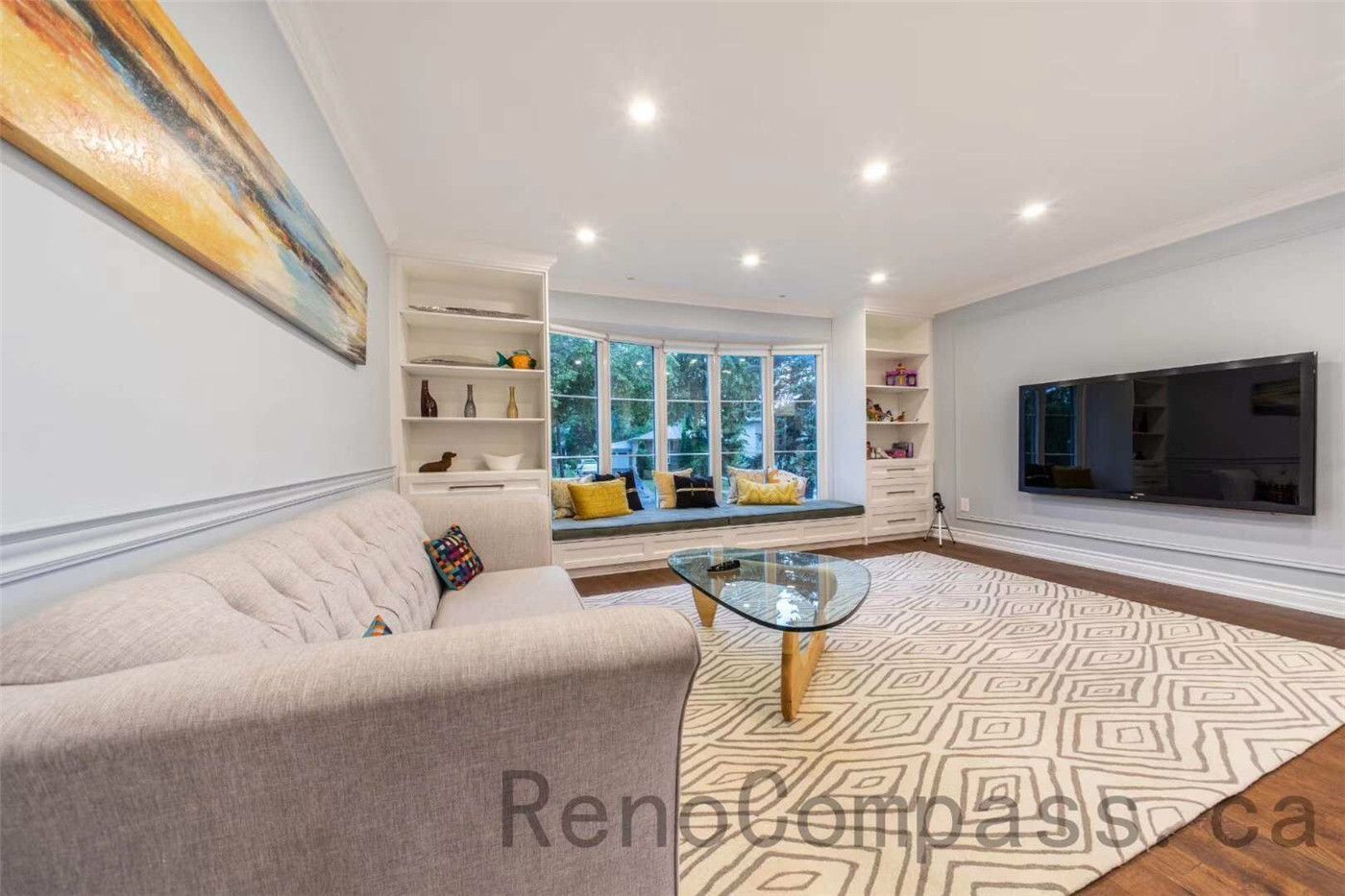This North York interior renovation showcases a bright and stylish living room featuring a custom window bench with built-in shelving and a sleek modern TV feature wall. Large bay windows bring in natural light while the open layout creates a comfortable space for family gatherings and relaxation. Completed by a trusted Toronto renovation company, the design blends contemporary finishes, recessed lighting, and warm hardwood flooring to create a welcoming and elegant living environment.