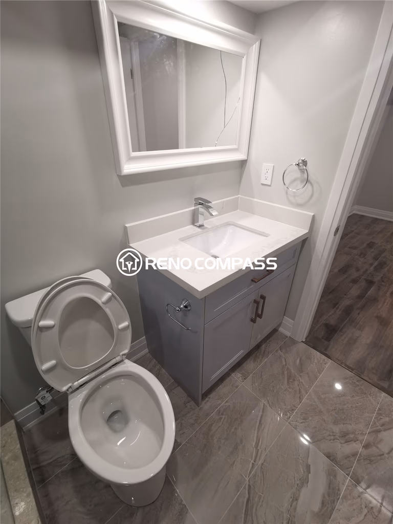 This Markham basement renovation features a fully upgraded bathroom with a modern vanity, quartz countertop, framed mirror, and new toilet installation. Large-format porcelain floor tiles enhance durability and water resistance while creating a sleek, contemporary look. The neutral color palette and clean finishing details maximize brightness and functionality within the compact basement bathroom layout. Completed by a professional Toronto renovation company, this project highlights quality fixture installation, detailed tile work, and practical basement bathroom design tailored for modern homes in the Greater Toronto Area.