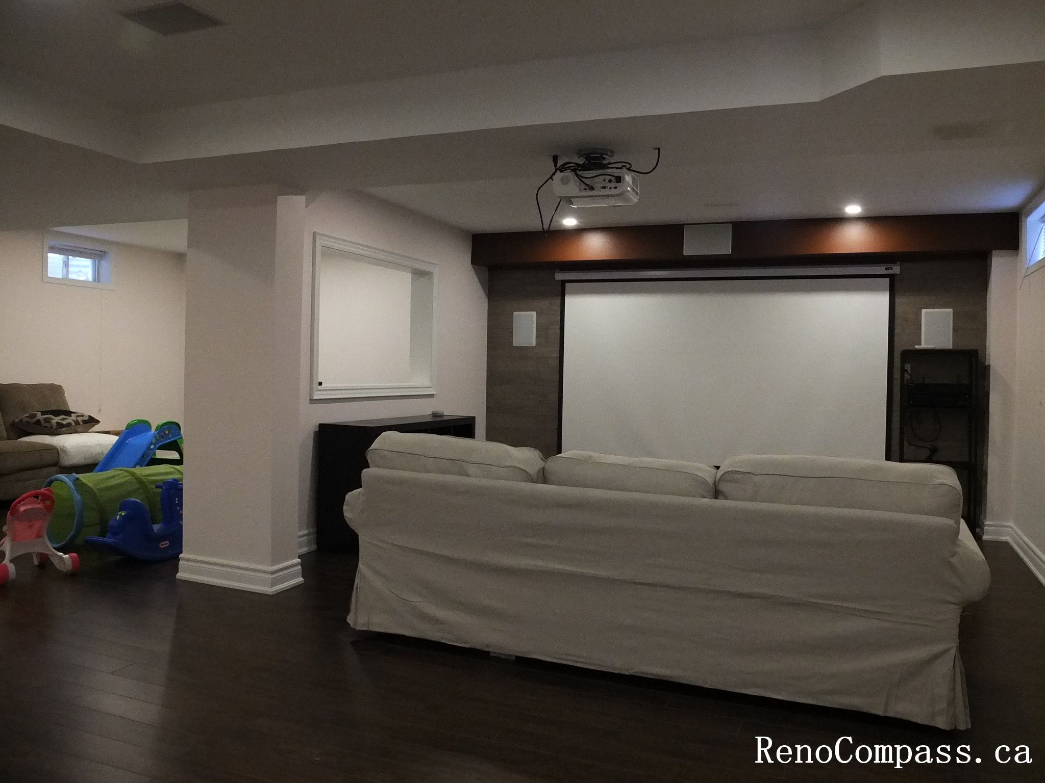 Modern basement interior renovation in Newmarket featuring a custom home theater setup, dark hardwood flooring, built-in shelving, recessed lighting, and a projector screen. Professionally completed by a Toronto Renovation Company to create a functional entertainment space for the whole family.