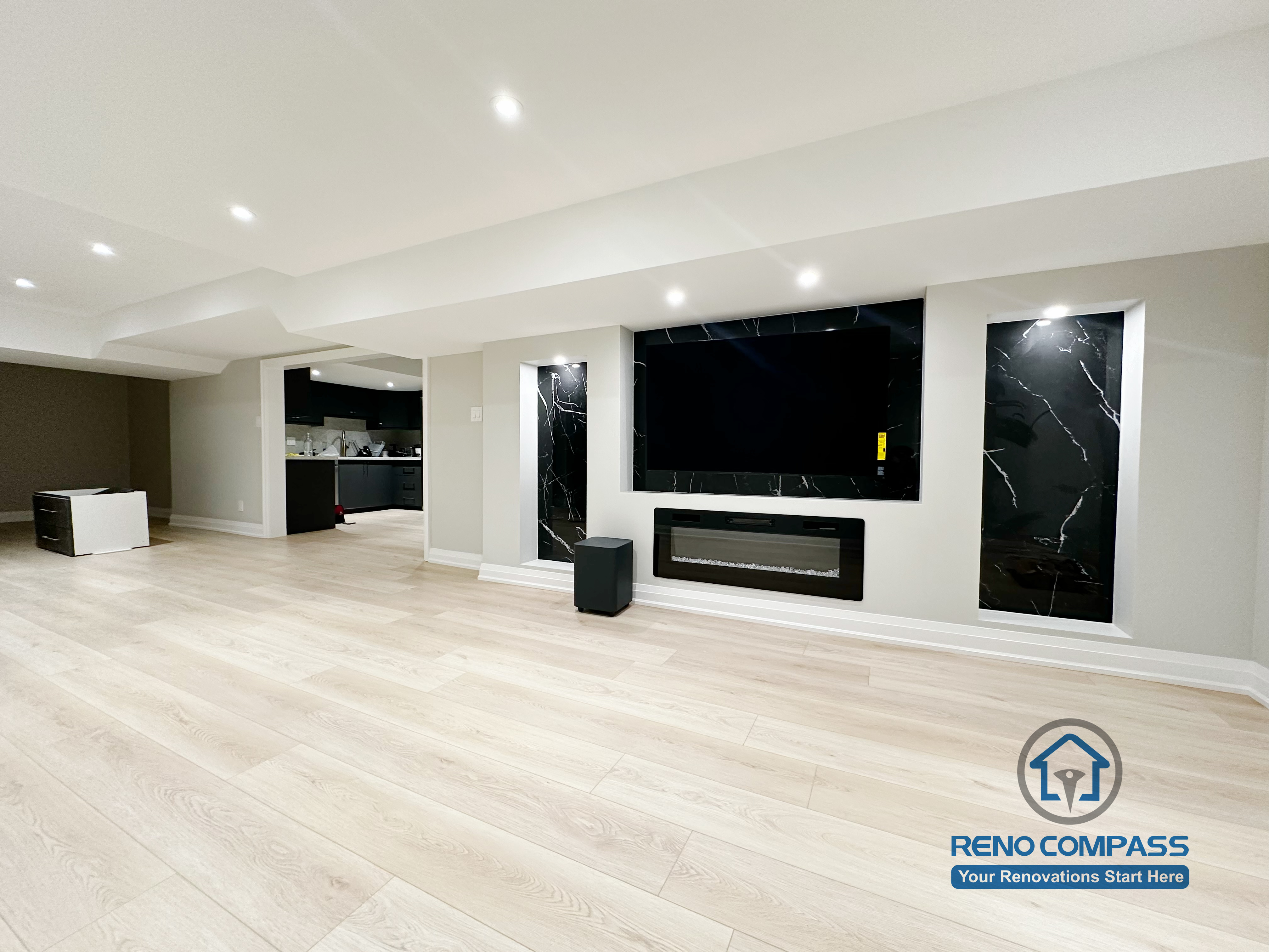 Finished basement renovation in Richmond Hill showcasing a modern feature wall with built-in fireplace, TV niche, black marble-style panels, and recessed lighting for a sleek entertainment space.
