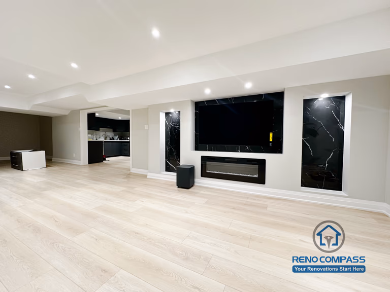 Finished basement renovation in Richmond Hill showcasing a modern feature wall with built-in fireplace, TV niche, black marble-style panels, and recessed lighting for a sleek entertainment space.