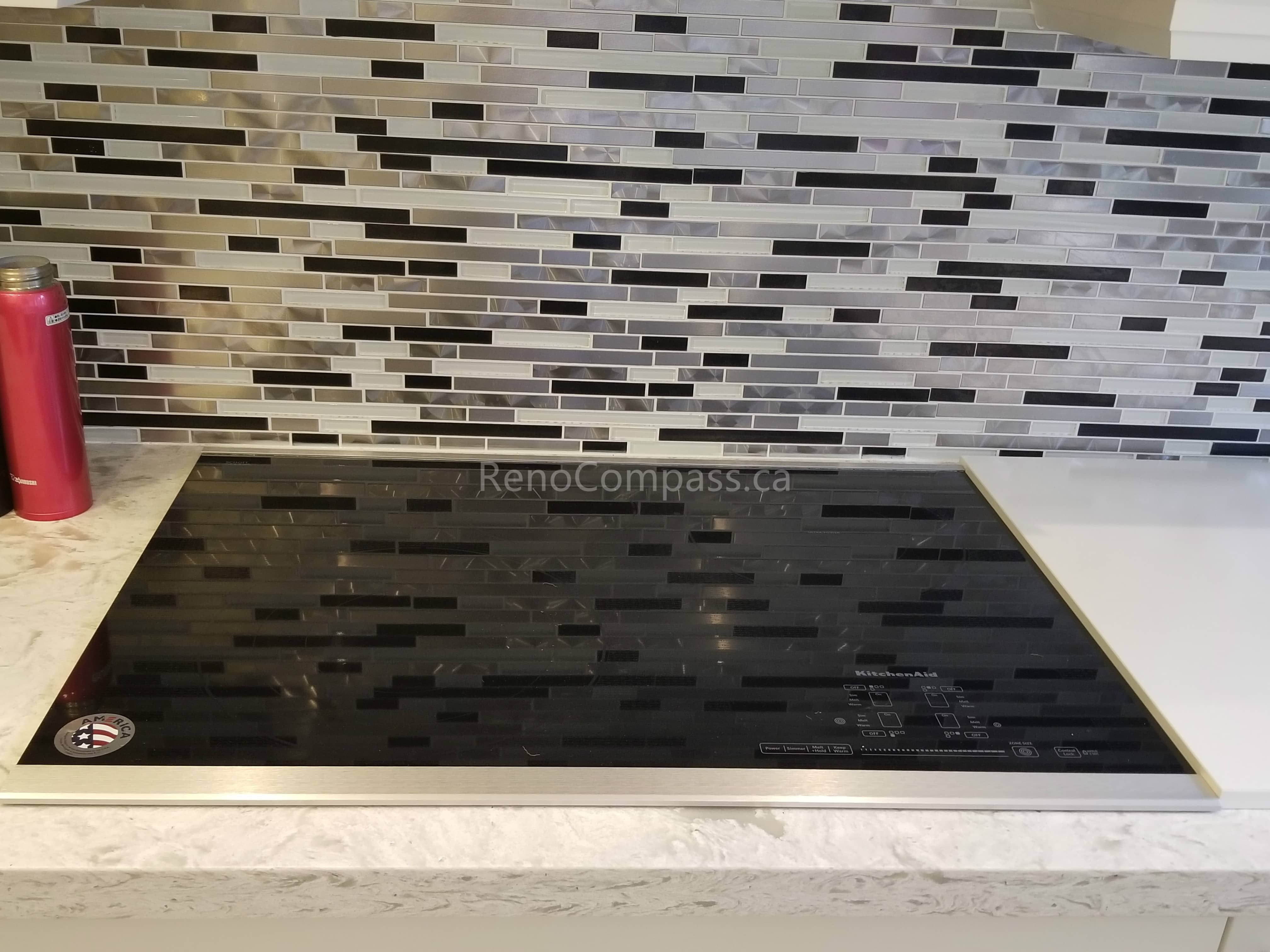 This Toronto interior renovation showcases a sleek modern kitchen upgrade featuring a built-in black glass induction cooktop, quartz countertop, and contemporary glass mosaic backsplash. The clean design, durable materials, and functional layout create a stylish and efficient cooking space, reflecting the quality craftsmanship of a professional Toronto renovation project by Reno Compass Inc.