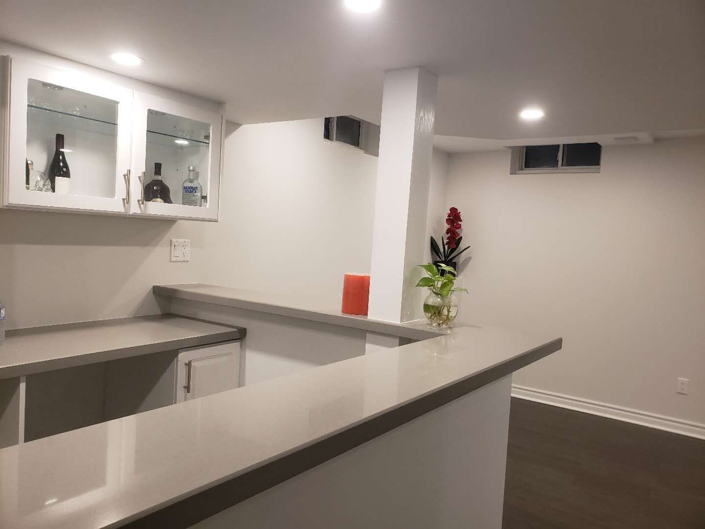 This Markham basement renovation features a clean and modern bar area with custom white cabinetry, a built-in sink, and a functional island countertop. Recessed pot lights and smooth ceiling finishes enhance brightness, while dark flooring adds contrast and warmth. The layout is designed to maximize usability and flow, making the basement ideal for entertaining, family gatherings, or multi-purpose living. This project reflects professional basement renovation standards in Markham, focusing on durability, lighting, and practical space planning.