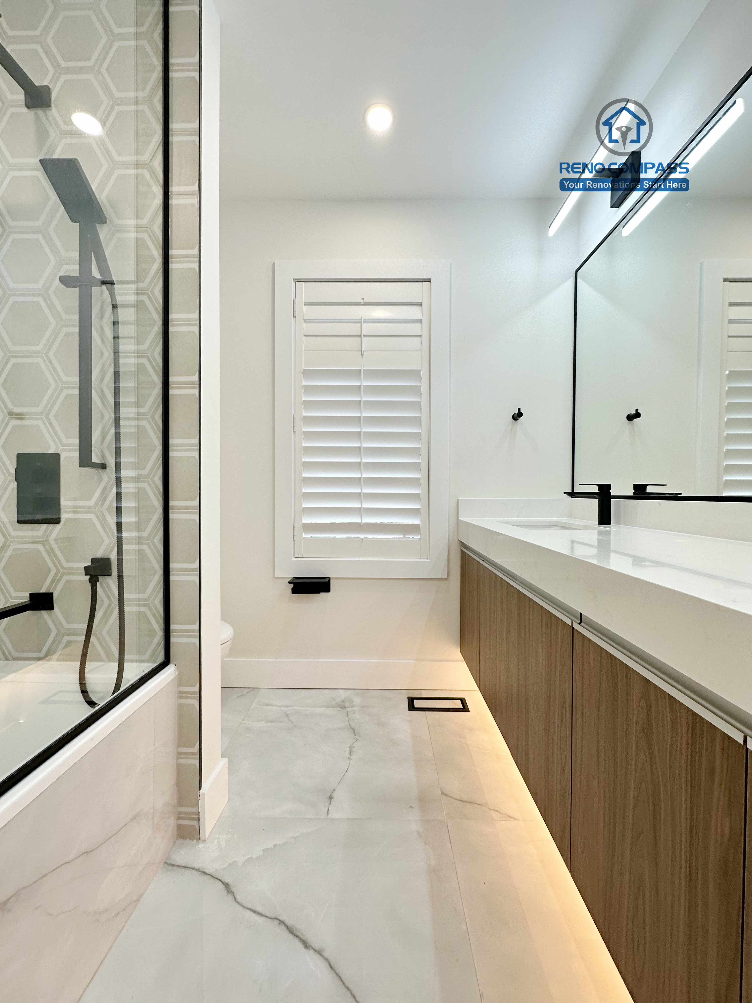 Modern bathroom renovation in Richmond Hill featuring a seamless layout between the glass-enclosed shower and a long floating double vanity, enhanced by matte black fixtures, hexagon tile accents, and integrated LED lighting.