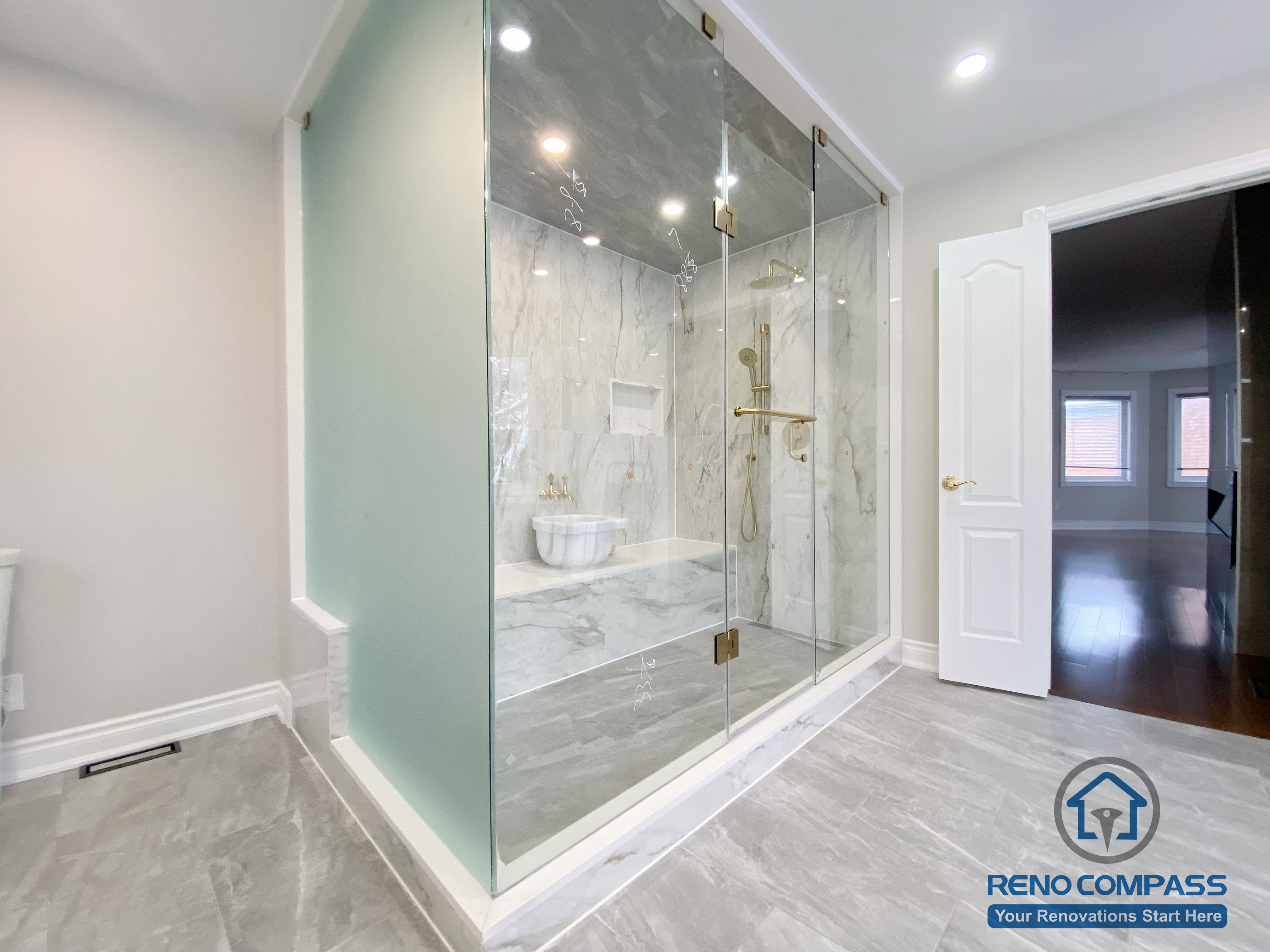 This Richmond Hill bathroom renovation showcases a bright and elegant design featuring a frameless glass shower enclosure, built-in bathtub, marble-style wall tiles, and gold-finish fixtures. The custom white vanity with integrated lighting mirror and large-format floor tiles enhance both functionality and visual openness. This project reflects high-quality craftsmanship and thoughtful layout planning for a modern bathroom renovation in Richmond Hill.