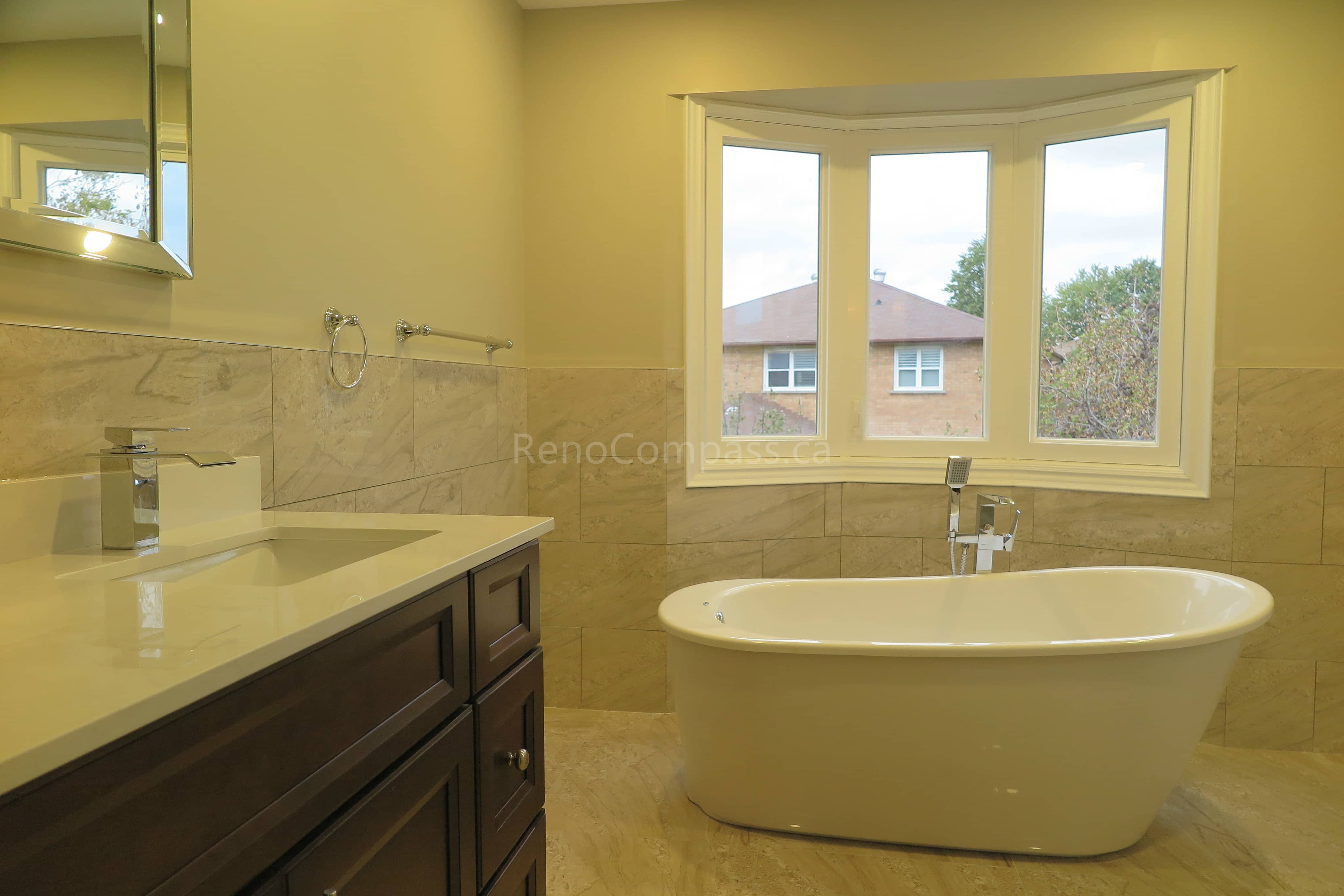 This Markham bathroom renovation features a modern freestanding soaking bathtub positioned beneath a large bay window, creating a bright and relaxing spa-like atmosphere. The space includes a custom vanity with quartz countertop, marble-style wall tiles, and updated fixtures that combine elegance with everyday functionality. Completed by Reno Compass, a trusted renovation contractor specializing in bathroom renovations and full interior remodeling across Markham and the Greater Toronto Area.
