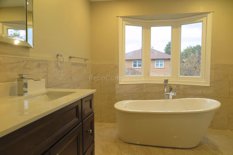 This Markham bathroom renovation features a modern freestanding soaking bathtub positioned beneath a large bay window, creating a bright and relaxing spa-like atmosphere. The space includes a custom vanity with quartz countertop, marble-style wall tiles, and updated fixtures that combine elegance with everyday functionality. Completed by Reno Compass, a trusted renovation contractor specializing in bathroom renovations and full interior remodeling across Markham and the Greater Toronto Area.