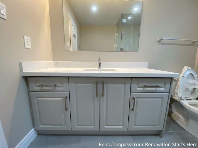 This Mississauga interior renovation features a clean and functional bathroom vanity with a quartz countertop and integrated storage cabinets. The soft gray cabinetry is paired with sleek hardware and a wide mirror, creating a bright and organized vanity area suitable for daily use. The streamlined design improves storage efficiency while maintaining a modern, timeless look that complements the overall interior renovation.