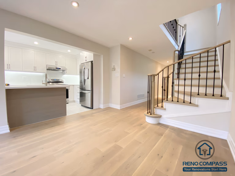 This Markham interior renovation showcases an open-concept layout that seamlessly connects the kitchen, living area, and staircase. The space features wide-plank hardwood flooring, a modern kitchen with white cabinetry and quartz countertops, and a refined staircase with hardwood treads and black metal railings. Recessed lighting enhances brightness and continuity throughout the main floor. Completed by a professional Toronto renovation company, this design improves circulation, visual balance, and everyday functionality for a Markham home.