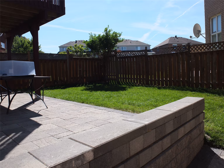 This Richmond Hill backyard landscaping renovation showcases a newly installed interlocking patio with clean stone steps and a raised retaining wall, creating a defined outdoor living space. The fresh green lawn and upgraded fencing enhance privacy and usability, making the backyard ideal for family gatherings and summer relaxation. Completed by a professional Toronto renovation company serving Richmond Hill and the GTA.