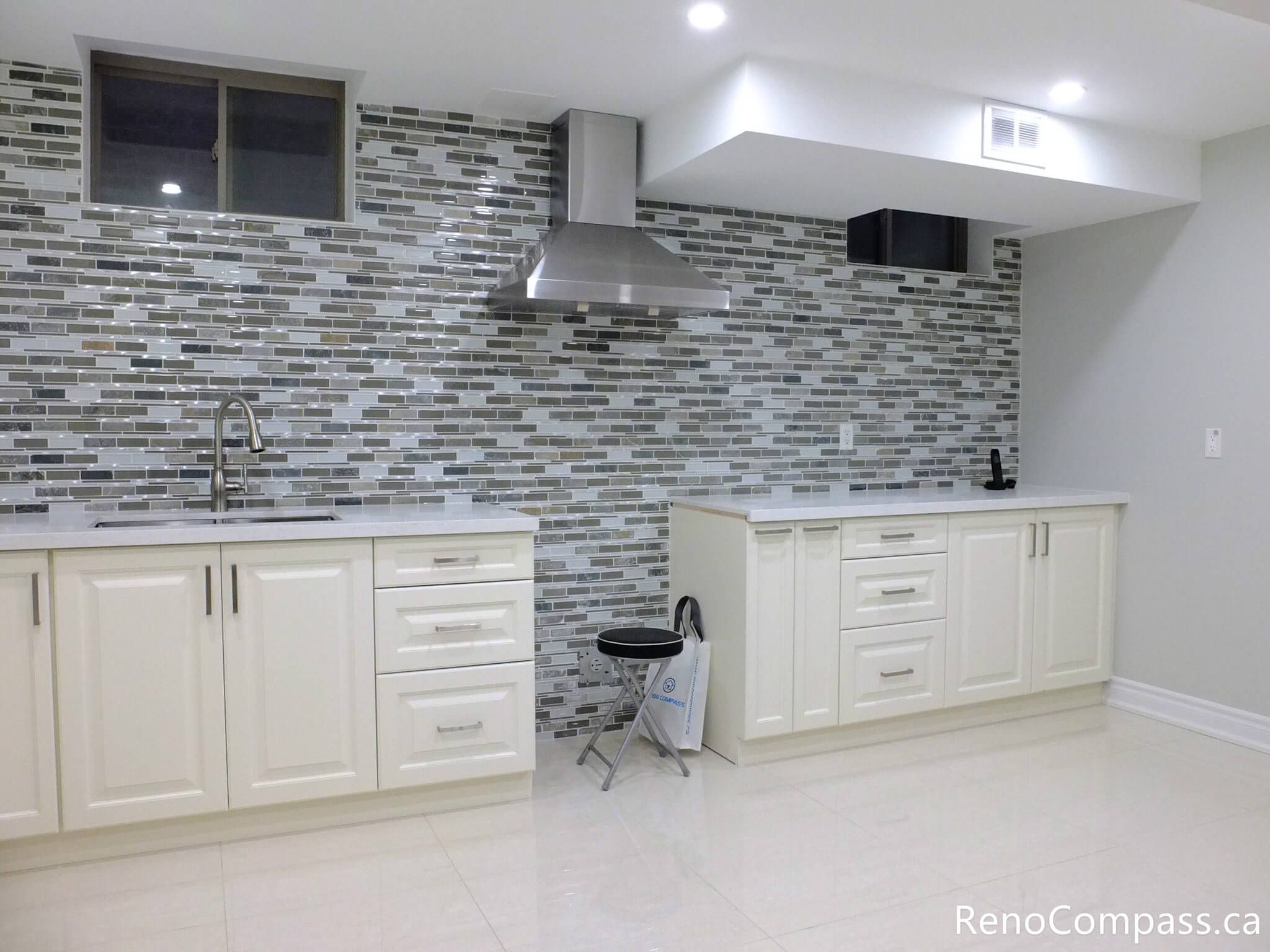 Modern basement kitchen installation in Markham featuring white shaker-style cabinetry, quartz countertop, stainless steel range hood, and full-height mosaic tile backsplash. The sleek layout and bright finishes enhance both functionality and visual appeal, making the basement a fully usable secondary living space. Completed by a professional Toronto renovation company, this project reflects attention to detail and high-quality craftsmanship.