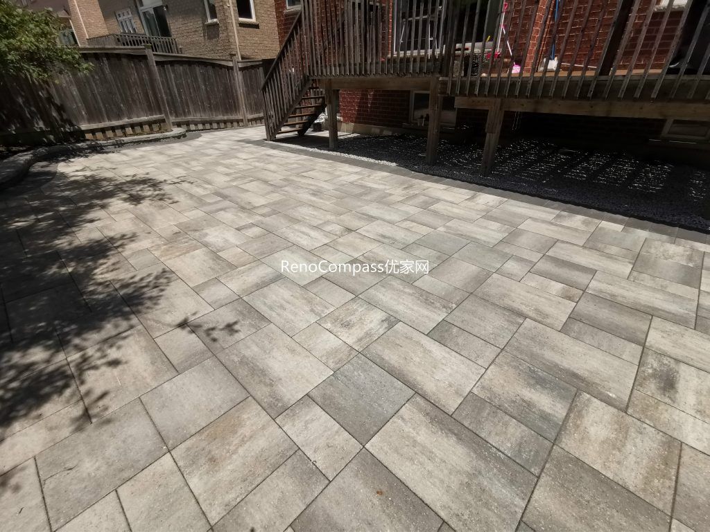 Modern backyard interlocking patio in Richmond Hill featuring elegant gray pavers and a curved stone border around the garden. The project seamlessly integrates with the wooden deck and stairs, creating a clean and functional outdoor space designed by RenoCompass for durability and style.