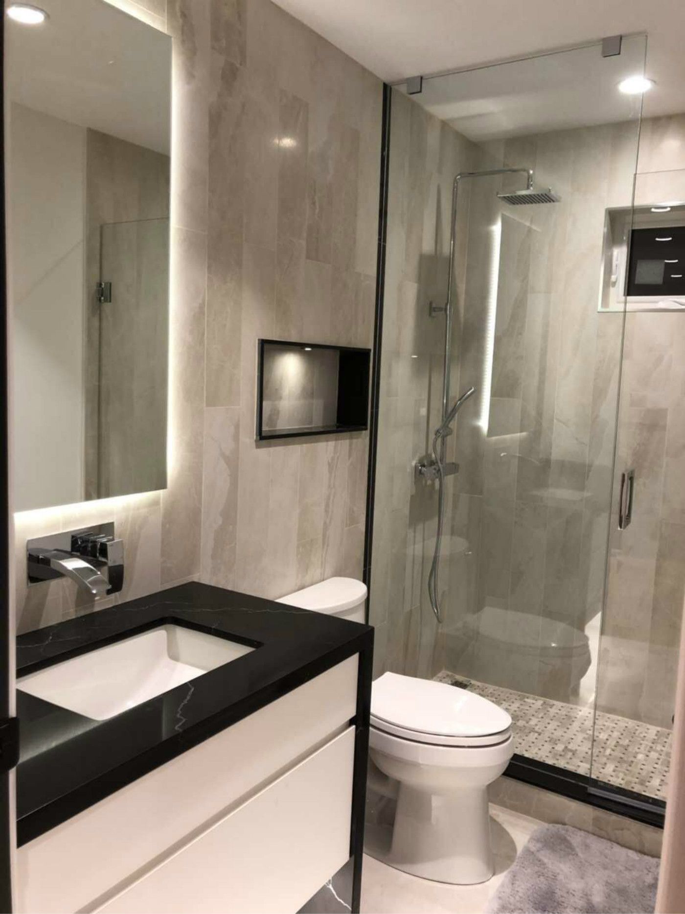 Contemporary bathroom renovation in Markham featuring a sleek glass shower enclosure, LED backlit mirror, black quartz vanity countertop, and marble-style wall tiles. This modern bathroom design combines functionality and elegance, creating a bright and luxurious space tailored for everyday comfort and long-term home value.