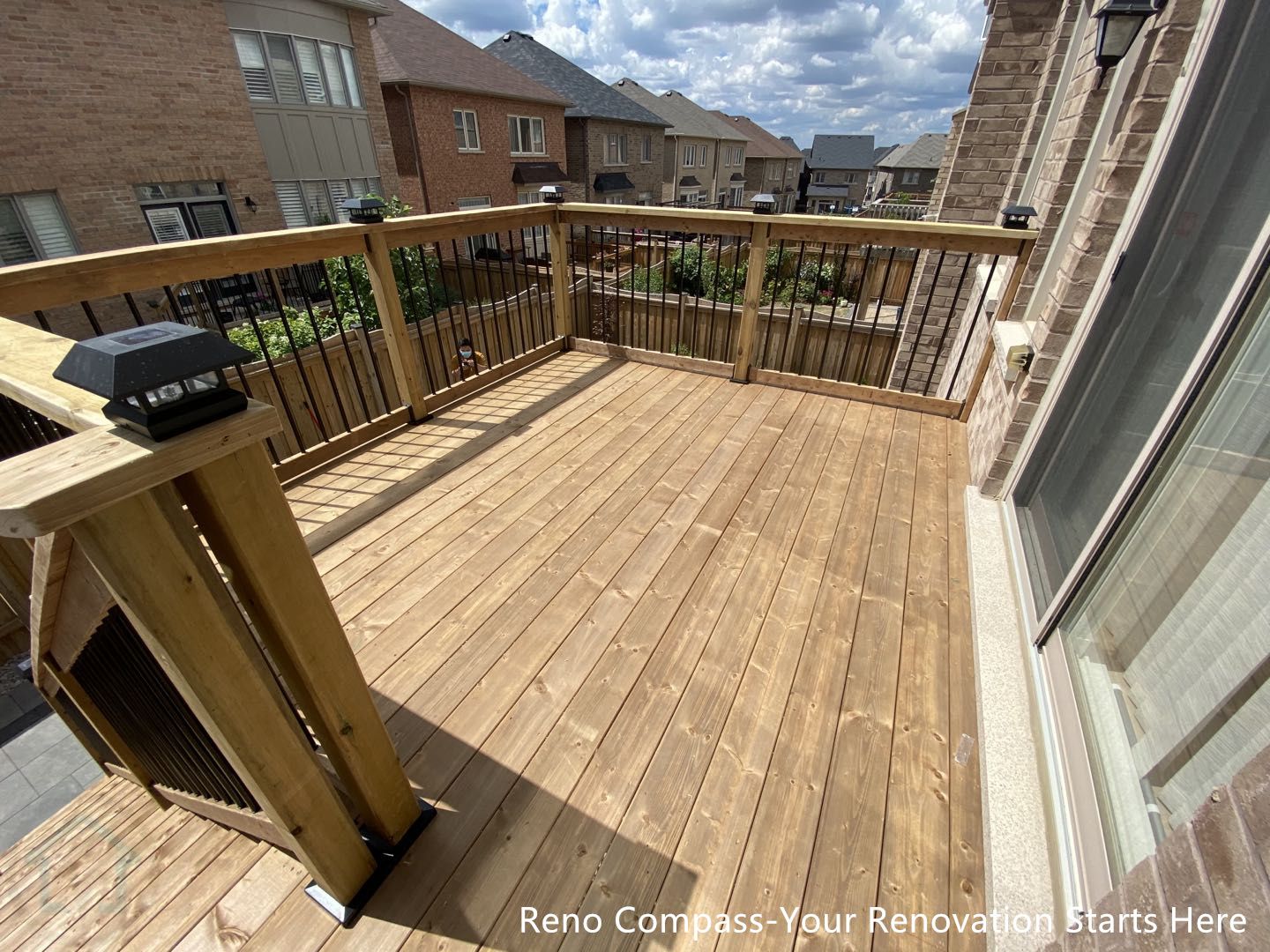 This image features the raised wooden deck platform completed as part of a Markham outdoor renovation project. The deck is constructed with pressure-treated wood boards, providing a durable and weather-resistant surface suitable for everyday outdoor use. Clean black metal railings add visual contrast while ensuring safety and openness, allowing unobstructed views across the backyard. Integrated post cap lighting enhances functionality during evening hours and improves overall usability. The balanced proportions and clean detailing create a practical, low-maintenance outdoor living space that connects seamlessly to the home. This custom deck construction was completed by Reno Compass, serving homeowners in Markham and the GTA.