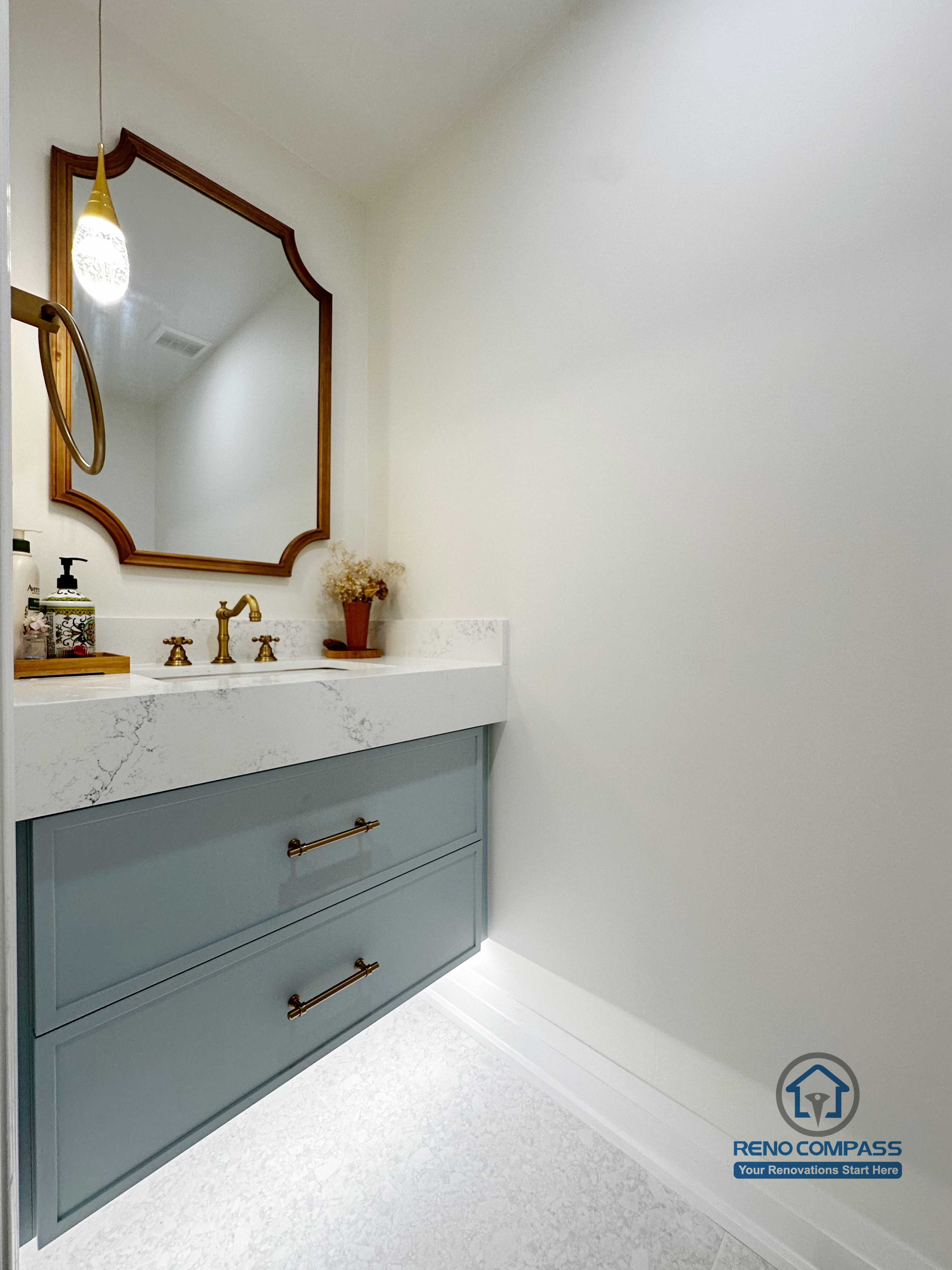 This Markham powder room renovation features a custom vanity with soft blue cabinetry, a quartz countertop, and warm brass fixtures. The curved mirror and minimal layout create a refined, elegant look while keeping the space bright, functional, and visually balanced.