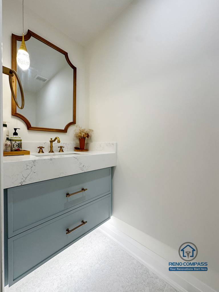 This Markham powder room renovation features a custom vanity with soft blue cabinetry, a quartz countertop, and warm brass fixtures. The curved mirror and minimal layout create a refined, elegant look while keeping the space bright, functional, and visually balanced.